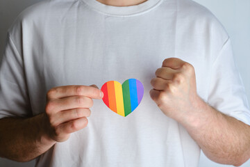 Rainbow heart from paper in man hands in white t-shirt. LGBT flag. LGBTQIA Pride Month in June....