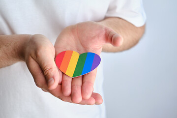 Rainbow heart from paper in man hands in white t-shirt. LGBT flag. LGBTQIA Pride Month in June. Lesbian Gay Bisexual Transgender. Gender equality. Human rights and tolerance. Rainbow flag