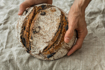 Fresh loaf of sourdough wholegrain spelt wheat bread in male hands. Natural linen fabric...