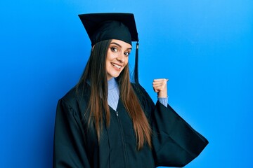 Beautiful brunette young woman wearing graduation cap and ceremony robe smiling with happy face...
