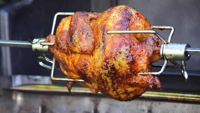 Roasted chicken rotating on spit on barbecue grill