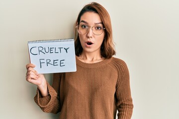 Young caucasian woman holding cruelty free message paper scared and amazed with open mouth for...