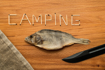 Matches and a piece of canvas with stockfish and combat knife on a wooden table. Matches form the...