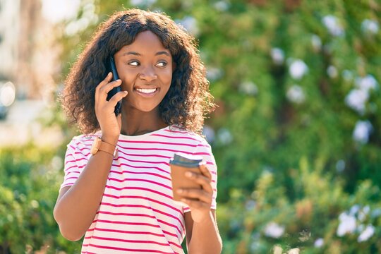 Young african american girl talking on the smartphone drinking coffee at the park.