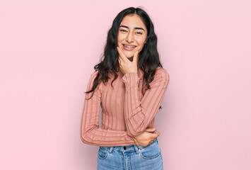 Hispanic teenager girl with dental braces wearing casual clothes looking confident at the camera smiling with crossed arms and hand raised on chin. thinking positive.
