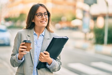 Young hispanic businesswoman drinking coffee holding binder at the city.