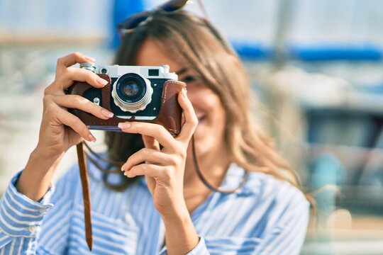 Young hispanic tourist woman smiling happy using vintage camera at the port.