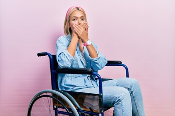 Beautiful blonde woman sitting on wheelchair shocked covering mouth with hands for mistake. secret...