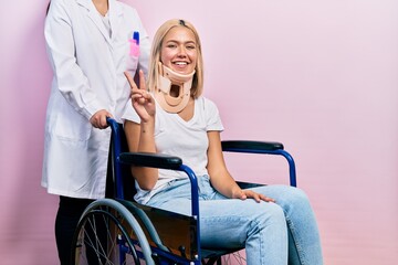 Beautiful blonde woman sitting on wheelchair with collar neck showing and pointing up with fingers...