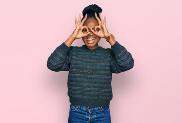 Young african american woman wearing casual clothes doing ok gesture like binoculars sticking...