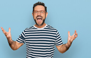 Naklejka premium Middle age man wearing casual clothes and glasses crazy and mad shouting and yelling with aggressive expression and arms raised. frustration concept.