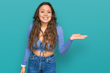 Young hispanic girl wearing casual clothes smiling cheerful presenting and pointing with palm of hand looking at the camera.