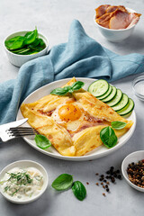 Crepe with egg, ham and cheese sprinkled with basil on a gray background.