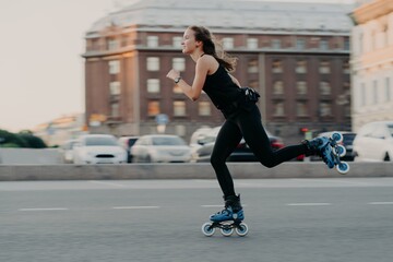 Athletic woman rides on rollers moves very fast dressed in active wear enjoys rollerblading being photographed in action poses at urban place engaged in extreme sport. Active lifestyle concept