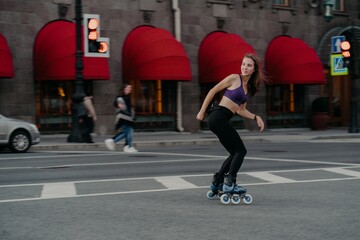 Slim sporty young woman uses rollerskates as mode of transportation in city enjoys favorite hobby...