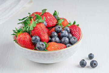 Portion of fresh ripe organic red garden strawberries and blueberries with juicy texture and sweetness, source of vitamin C and dietary minerals served in bowl on white wooden background. Horizontal