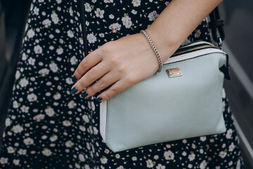 Woman's hand with manicure and bracelet holds a handbag. Girl in a dress with a handbag. Hand with manicure and jewelry holding a blue handbag.