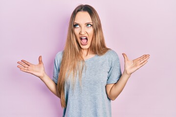 Young blonde girl wearing casual t shirt crazy and mad shouting and yelling with aggressive...
