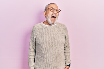 Handsome senior man with beard wearing casual sweater and glasses angry and mad screaming frustrated and furious, shouting with anger. rage and aggressive concept.