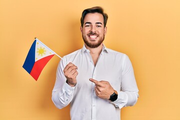 Handsome caucasian man with beard holding philippines flag smiling happy pointing with hand and...