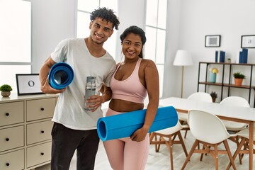 Fototapeta na wymiar Young latin sporty couple smiling happy holding yoga mat and bottle ofa water at home