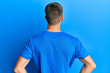 Young caucasian man wearing casual blue t shirt standing backwards looking away with arms on body