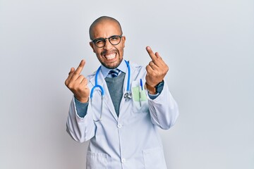 Hispanic adult man wearing doctor uniform and stethoscope showing middle finger doing fuck you bad...