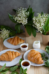 Fresh crispy croissants on a wooden table against a background of spring flowers.