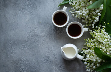 White cup with black coffee and flowers on a gray background. Top view, copy space