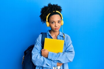 Young african american girl wearing student backpack and headphones holding book clueless and confused expression. doubt concept.