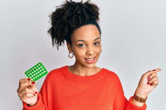 Young african american girl holding birth control pills smiling happy pointing with hand and finger to the side