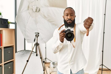 African american photographer man working at photography studio looking unhappy and angry showing rejection and negative with thumbs down gesture. bad expression.