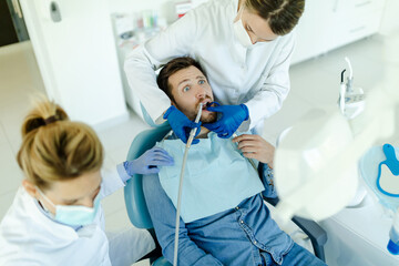 Female dentist drilling tooth to male patient in dental chair.