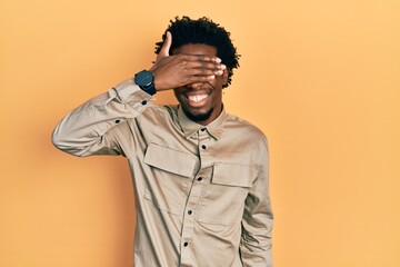 Young african american man wearing casual clothes and glasses smiling and laughing with hand on face covering eyes for surprise. blind concept.