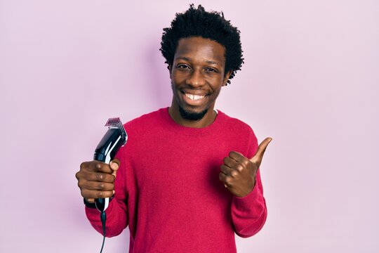 Young african american man holding razor smiling happy and positive, thumb up doing excellent and approval sign