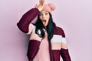 Young hispanic woman wearing wool winter sweater and cap surprised with hand on head for mistake,...