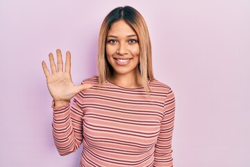 Beautiful hispanic woman wearing casual striped sweater showing and pointing up with fingers number five while smiling confident and happy.