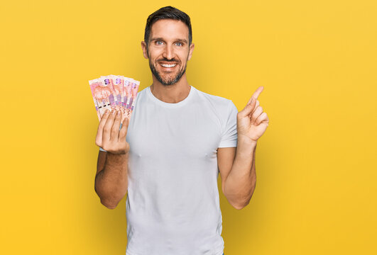 Handsome man with beard holding south african 50 rand banknotes smiling happy pointing with hand and finger to the side