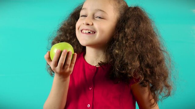 Happy Kid Makes A Choice In Favor Of A Green Apple. Funny Child On Turquoise Background Of Holding A Green Apple And Orange And Choice Healthy Eating Between Fruit And Orange.