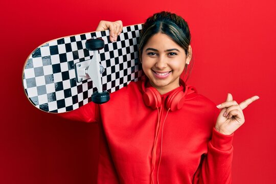 Young latin woman holding skate smiling happy pointing with hand and finger to the side