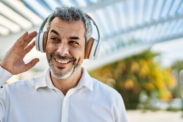 Middle age grey-haired man smiling happy using headphones at the city.