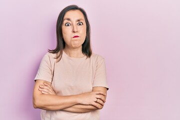 Fototapeta premium Middle age hispanic woman with arms crossed gesture puffing cheeks with funny face. mouth inflated with air, catching air.