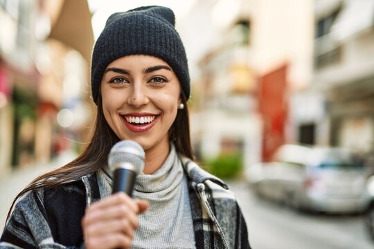 Young hispanic woman smiling happy using microphone at the city.