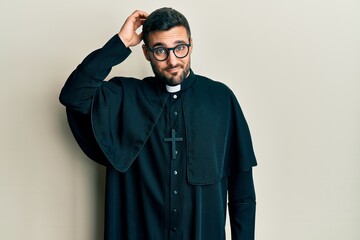 Obraz premium Young hispanic man wearing priest uniform standing over white background confuse and wonder about question. uncertain with doubt, thinking with hand on head. pensive concept.