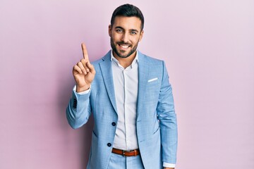Young hispanic businessman wearing business jacket showing and pointing up with finger number one while smiling confident and happy.