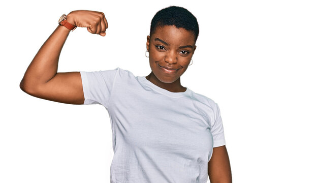 Young african american woman wearing casual white t shirt strong person showing arm muscle, confident and proud of power