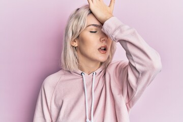 Young blonde girl wearing casual clothes surprised with hand on head for mistake, remember error....