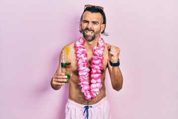 Young hispanic man wearing swimsuit and hawaiian lei drinking tropical cocktail angry and mad...