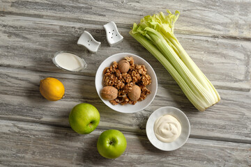 Ingredients for making a Waldorf salad made of celery, apples and walnuts on a light wooden background in a rustic style