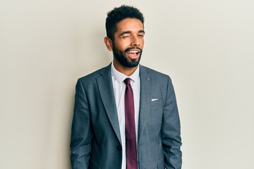 Handsome hispanic man with beard wearing business suit and tie winking looking at the camera with...